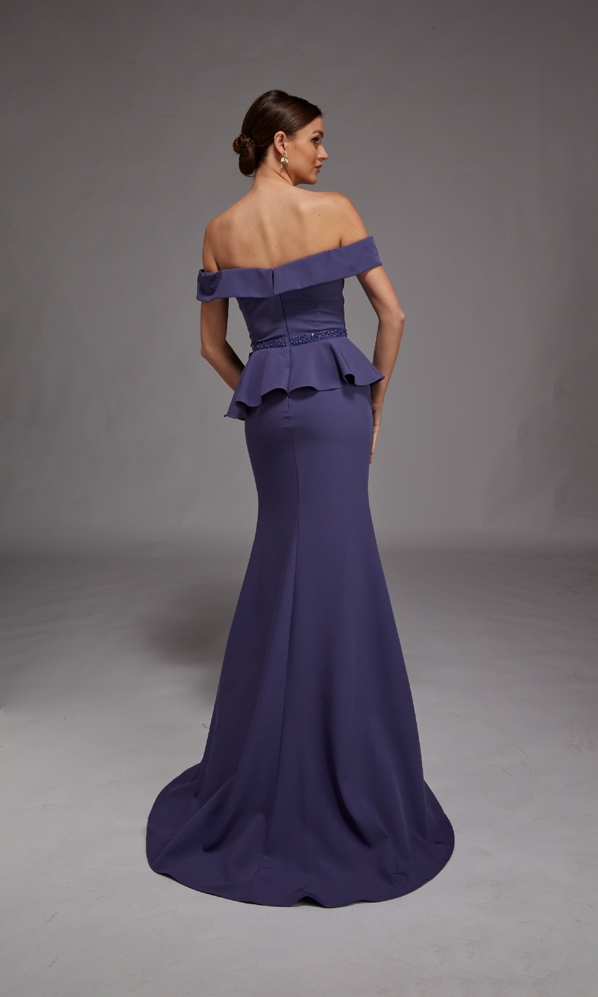 A woman stands with her back to the camera in a studio, wearing the Alyce 27829 long formal dress—an off-the-shoulder, floor-length gown with peplum detail, perfect for special occasions.